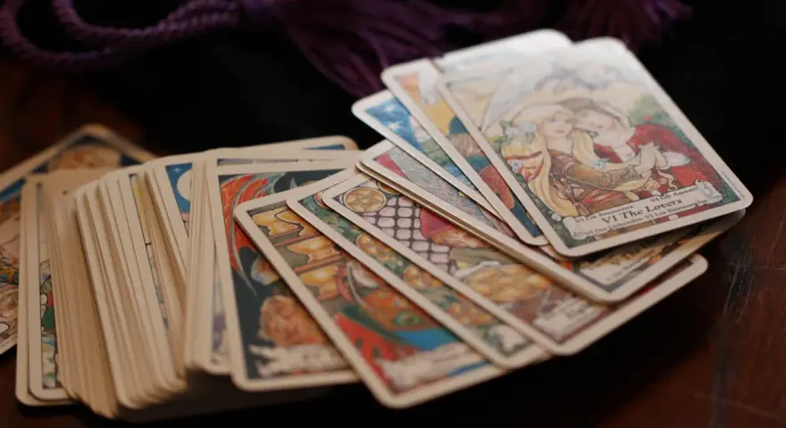 Karty tarota ułożone na drewnianym stole. Wśród nich widać kartę "Kochankowie". Sprawdź swój tarot tygodniowy skorpion.