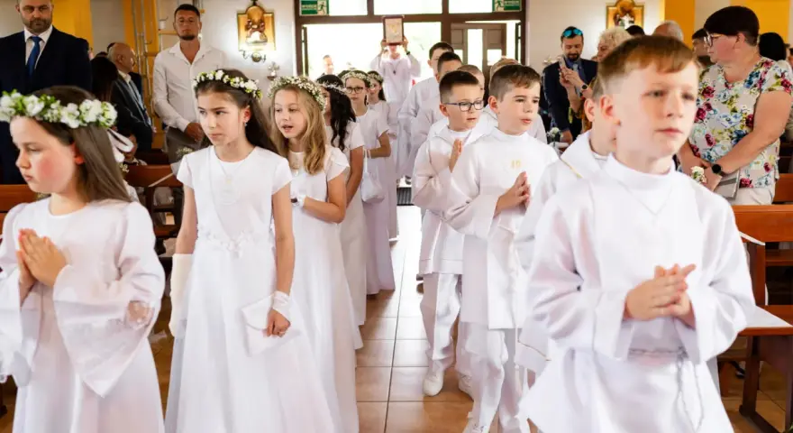 Dzieci w białych strojach, dziewczynki z wiankami, chłopcy z medalikami, przygotowują się do przyjęcia sakramentu, co to jest komunia święta.