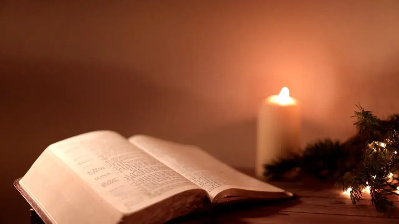 Otwarta Biblia, płonąca świeca i gałązka choinki tworzą nastr&oacute;j do szukania pocieszających cytat&oacute;w z Biblii.