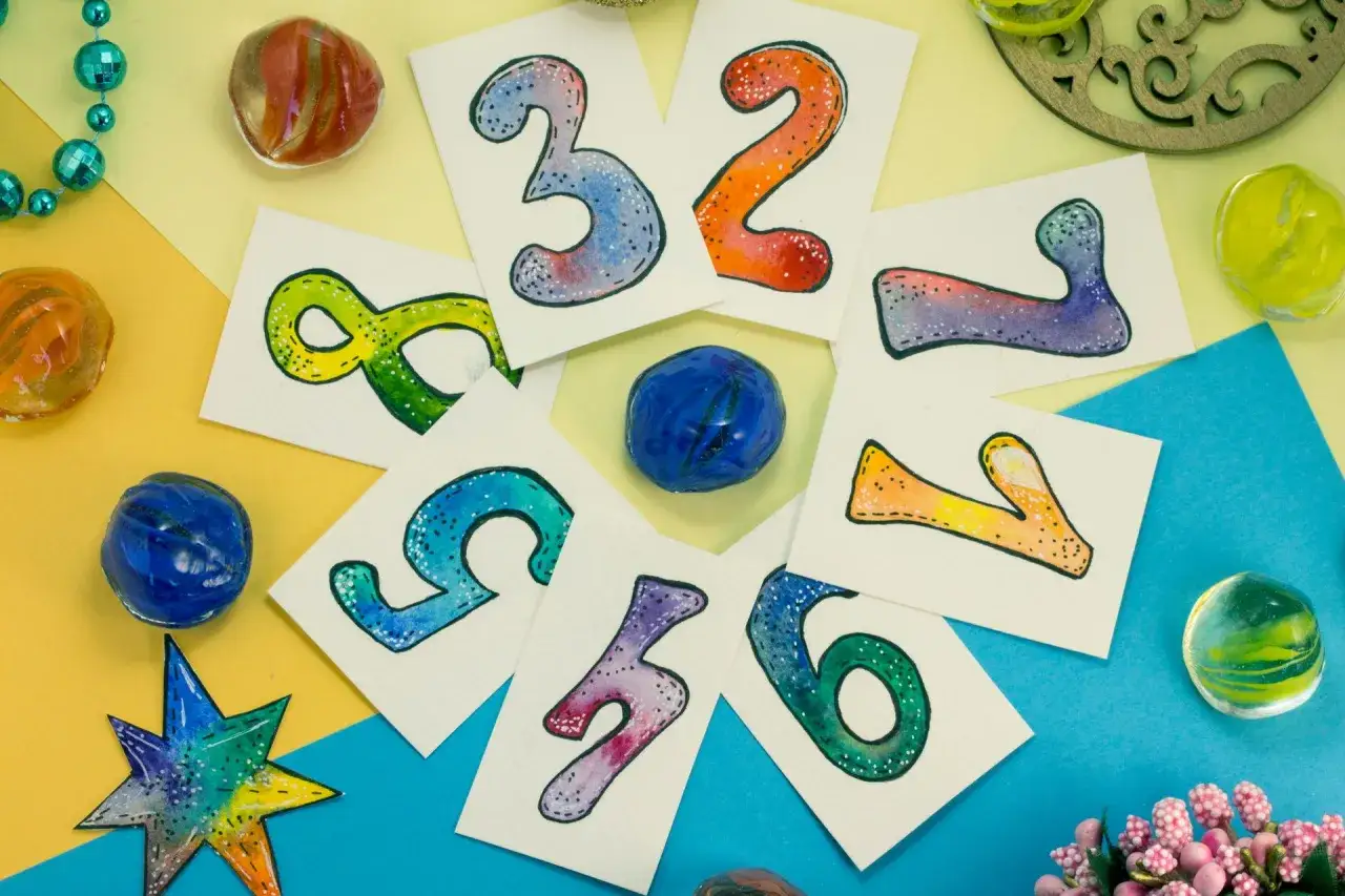 Kolorowe karty z cyframi, jak 3, 2, 8, 5, 7, 6, 1, 4 i 11, otoczone szklanymi kulkami i koralikami.