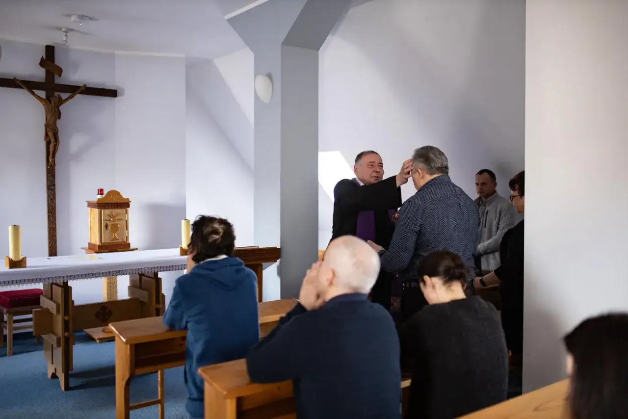 Kapłan udziela błogosławieństwa w kaplicy. Wierni klęczą, szukając miejsca, gdzie odbyć spowiedź generalną.