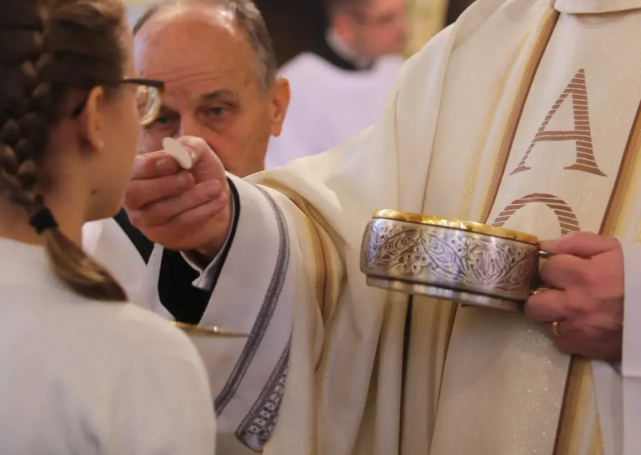 Kapłan udziela Komunii Świętej. To ważny moment, gdy wierni przyjmują Ciało Chrystusa.