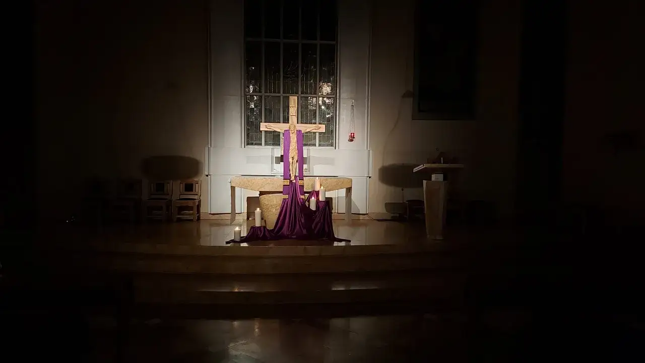 Drewniany krzyż z postacią Chrystusa, ozdobiony fioletową tkaniną i świecami, tworzy nastrój krótkiej drogi krzyżowej.