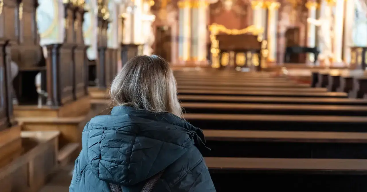 Kobieta w kościele, zadumana nad tym, czy tajemnice szczęścia trzeba odmawiać na klęcząco.