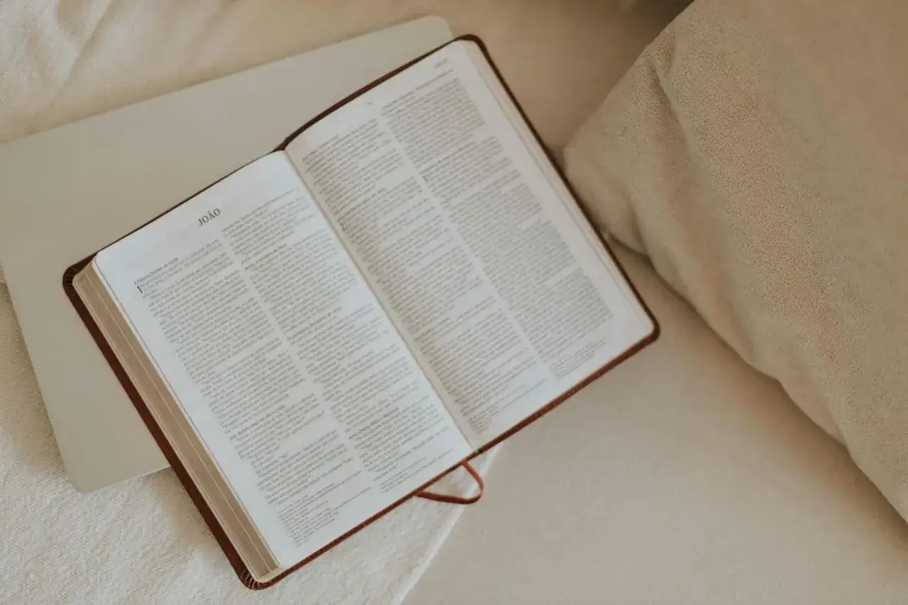 Modlitwa przed czytaniem Pisma Świętego. Otwarta Biblia leży na jasnym tle, obok poduszki.