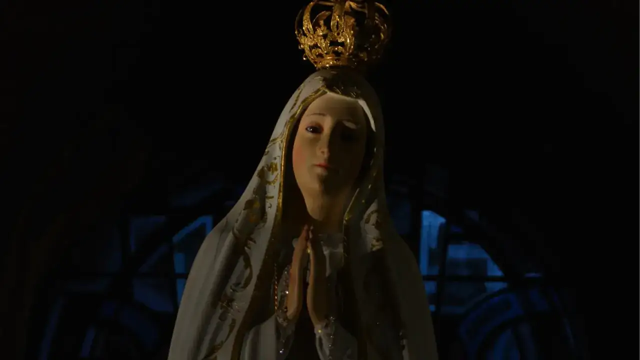 Figurka Matki Bożej z Fatimy, w koronie i welonie, z dłońmi złożonymi do modlitwy. Jej spojrzenie zdaje się ostrzegać.