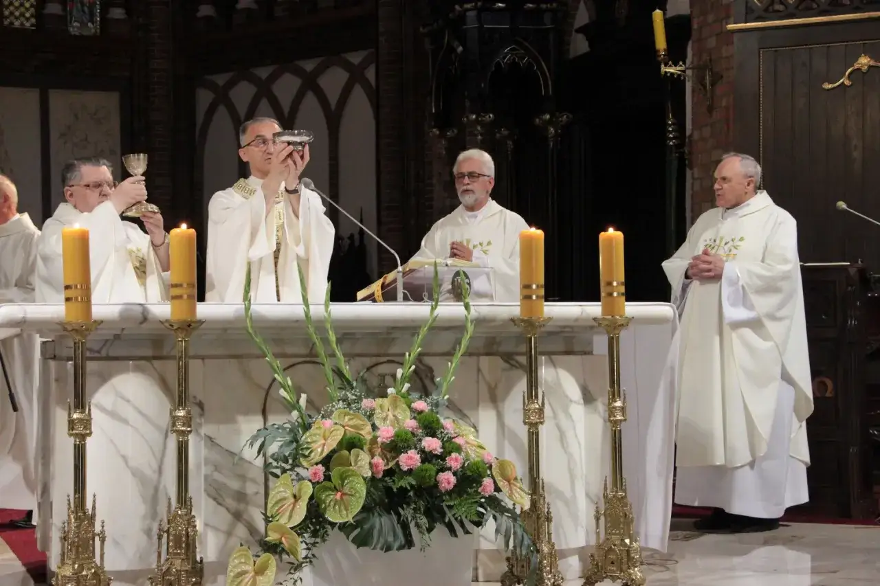 Kapłani podczas mszy świętej, wznoszący kielichy. W tle ołtarz z kwiatami i świecami. Modlitwa za kapłanów.