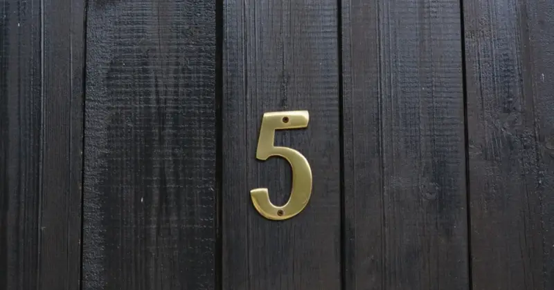 Złota cyfra 5 na ciemnej, drewnianej desce. Numerologiczna 3 i 5 symbolizują zmianę i wolność.