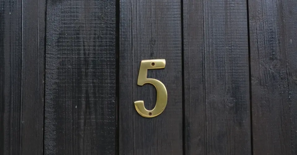 Złota cyfra 5 na ciemnej, drewnianej desce. Numerologiczna 3 i 5 symbolizują zmianę i wolność.